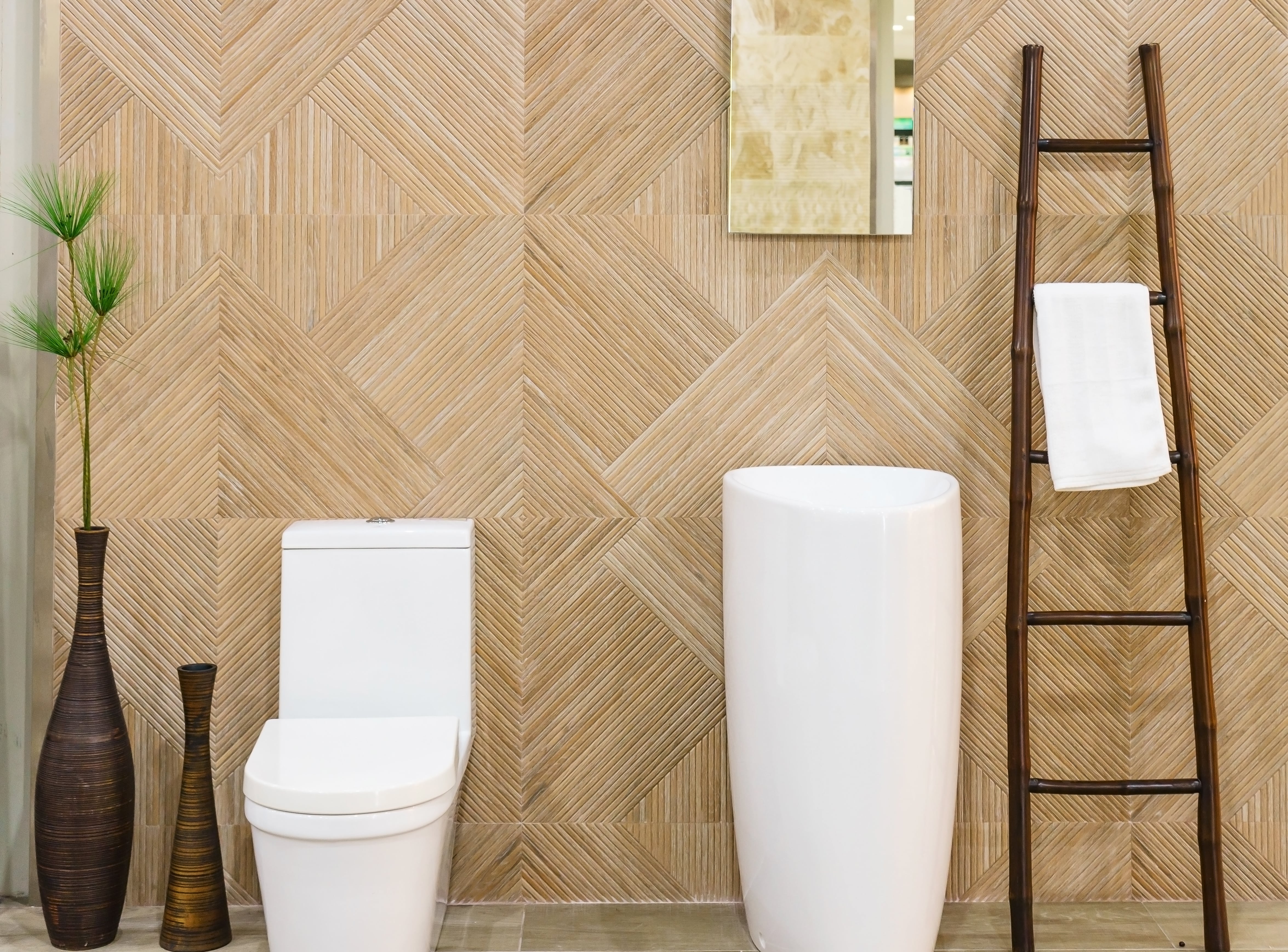 Mid-century modern bathroom with wood-grain floor tiles, white pedestal sink and toilet, ladder towel rank, and plants