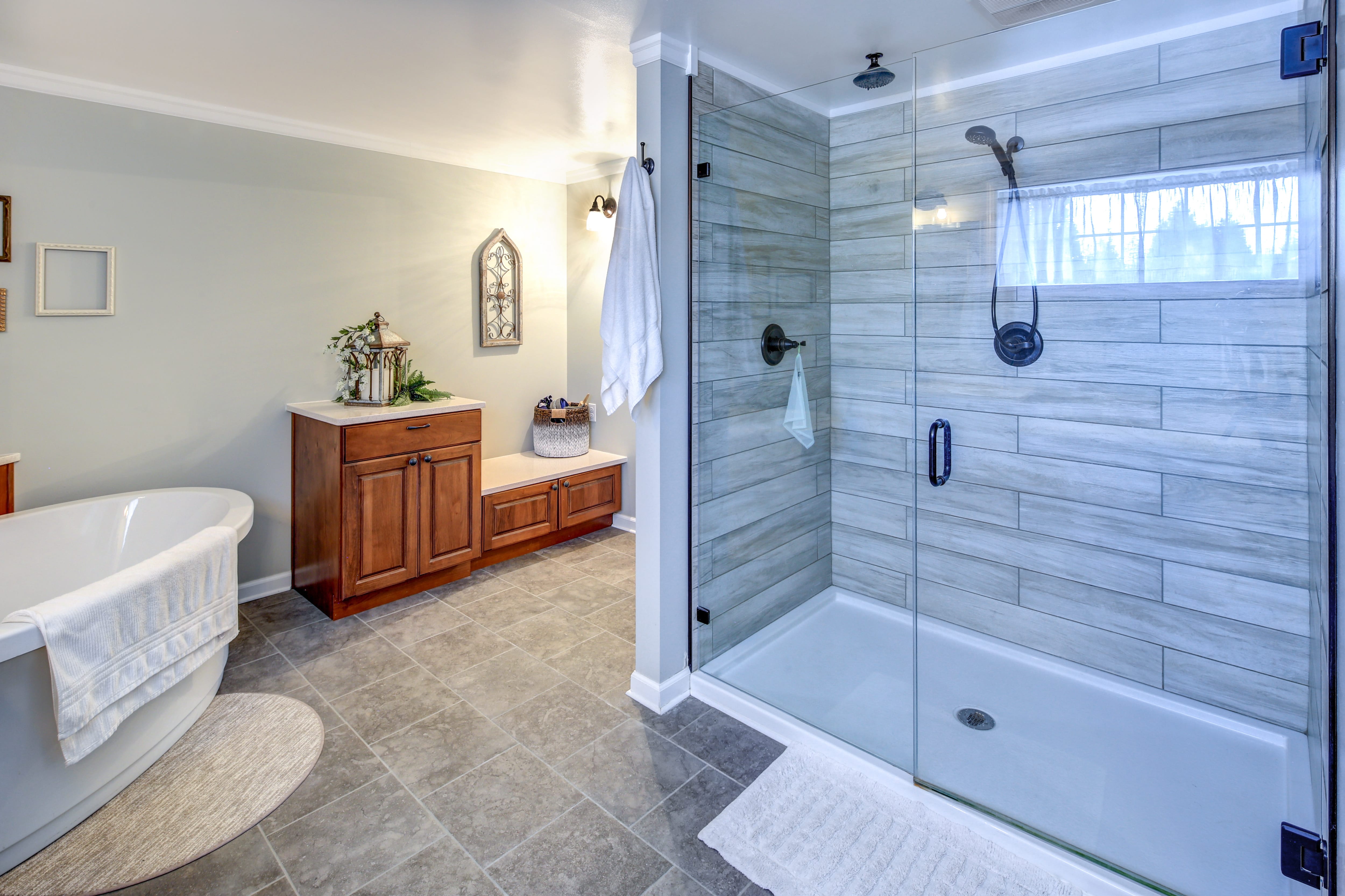 Spa-like bathroom with gray tiled shower and floor, freestanding tub, and brown vanity 