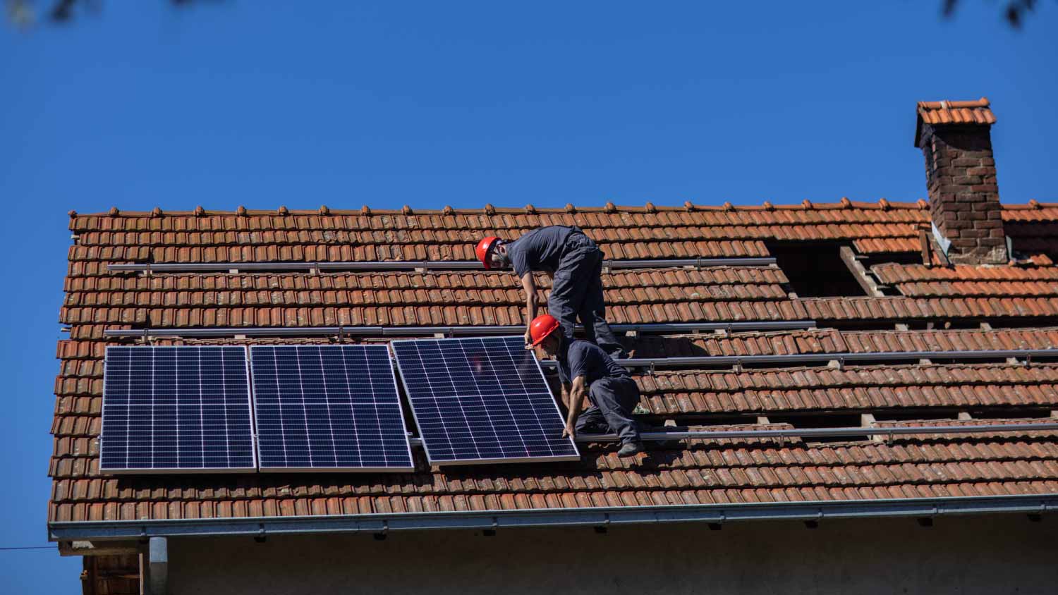 Workers mounting solar panels on roof of house
