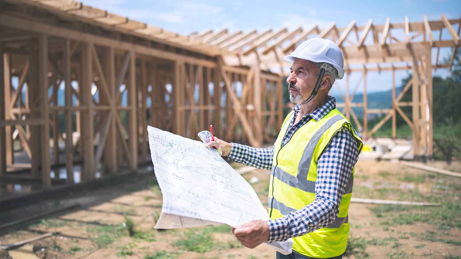 Architect wearing a helmet reviewing blueprints at construction site 