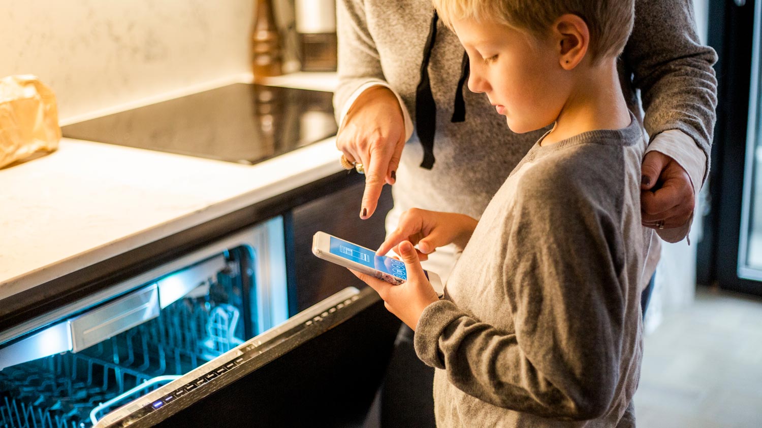  A boy using a smartphone to start the dishwasher