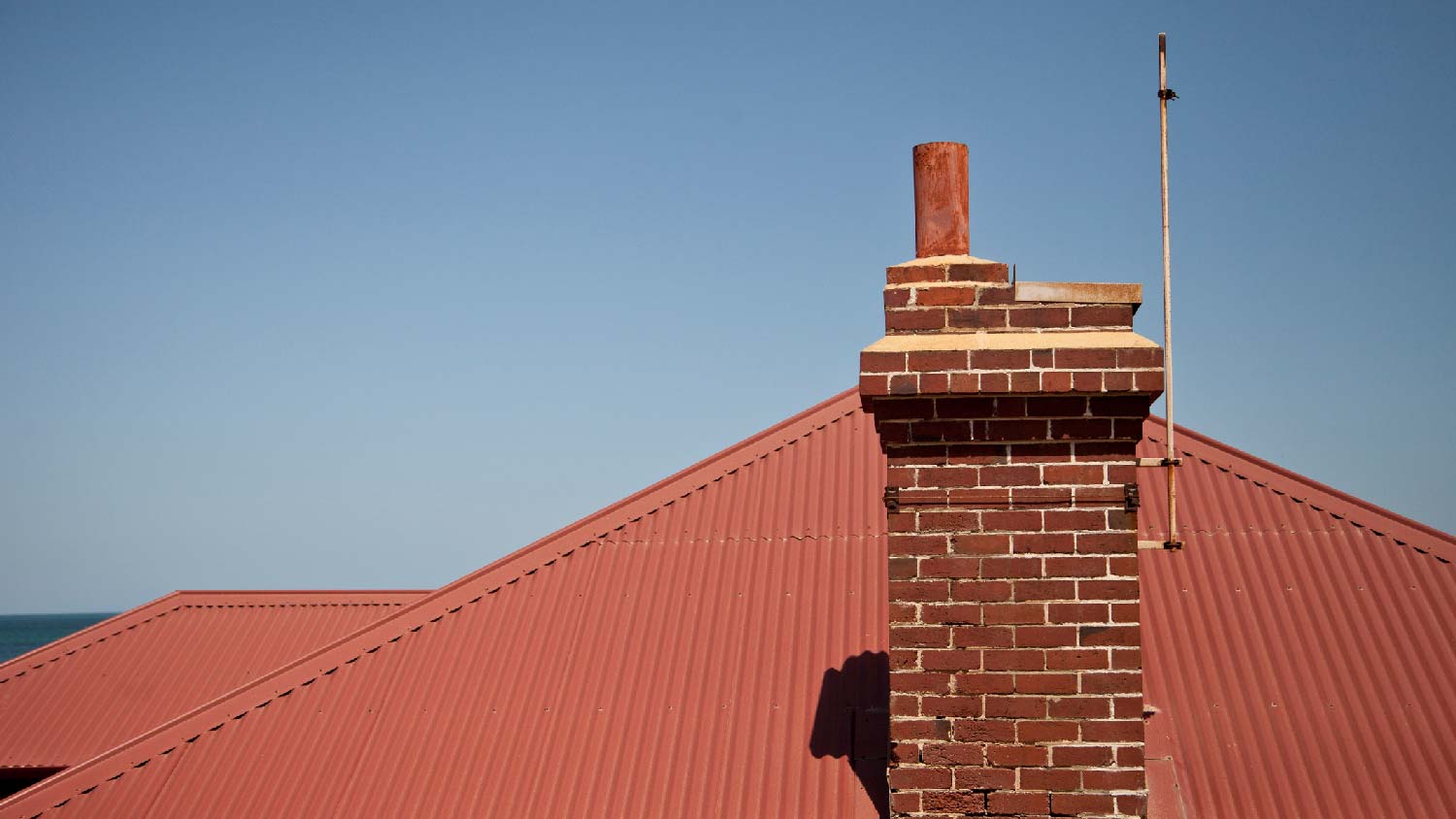 A brick chimney on a house with a metal roof