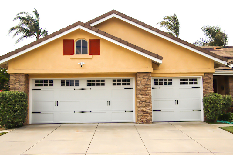forward view of yellow and brick house with double and single garage and concrete driveway