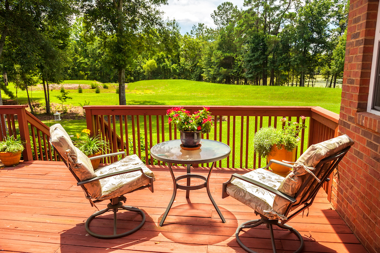 a cedar deck with two patio chairs and a small table overlooking a lush green yard