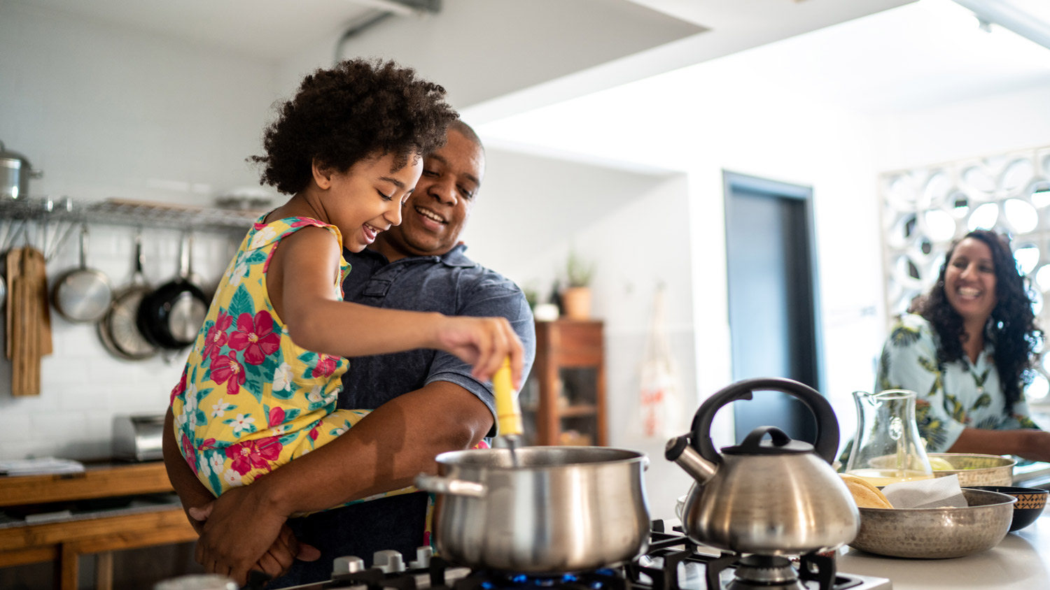 Girl in father's arms helping him cooking at home