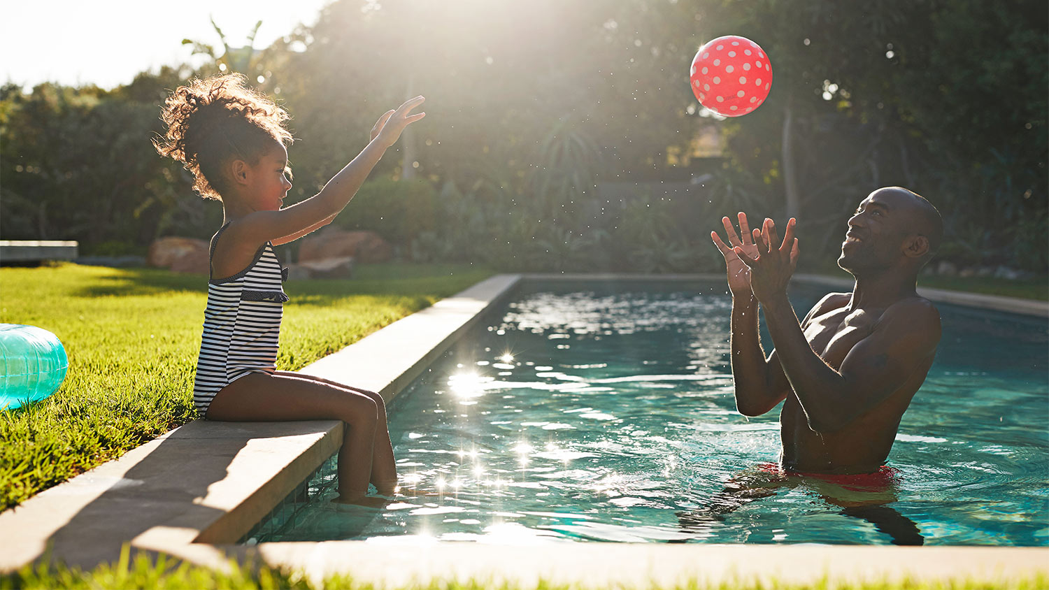 Young girl playing with red ball with her father in pool