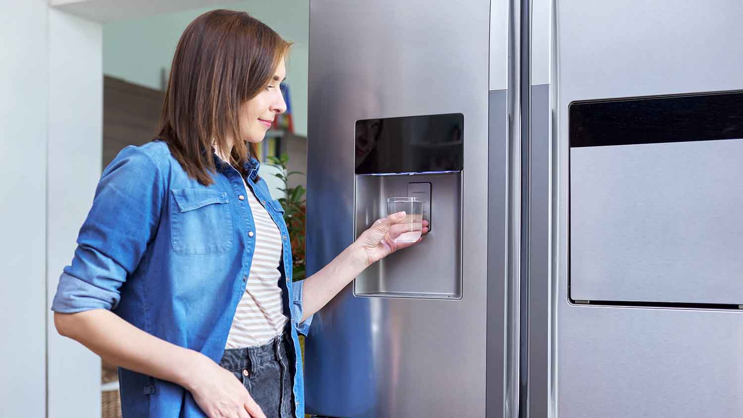 Woman using fridge water dispenser at home 