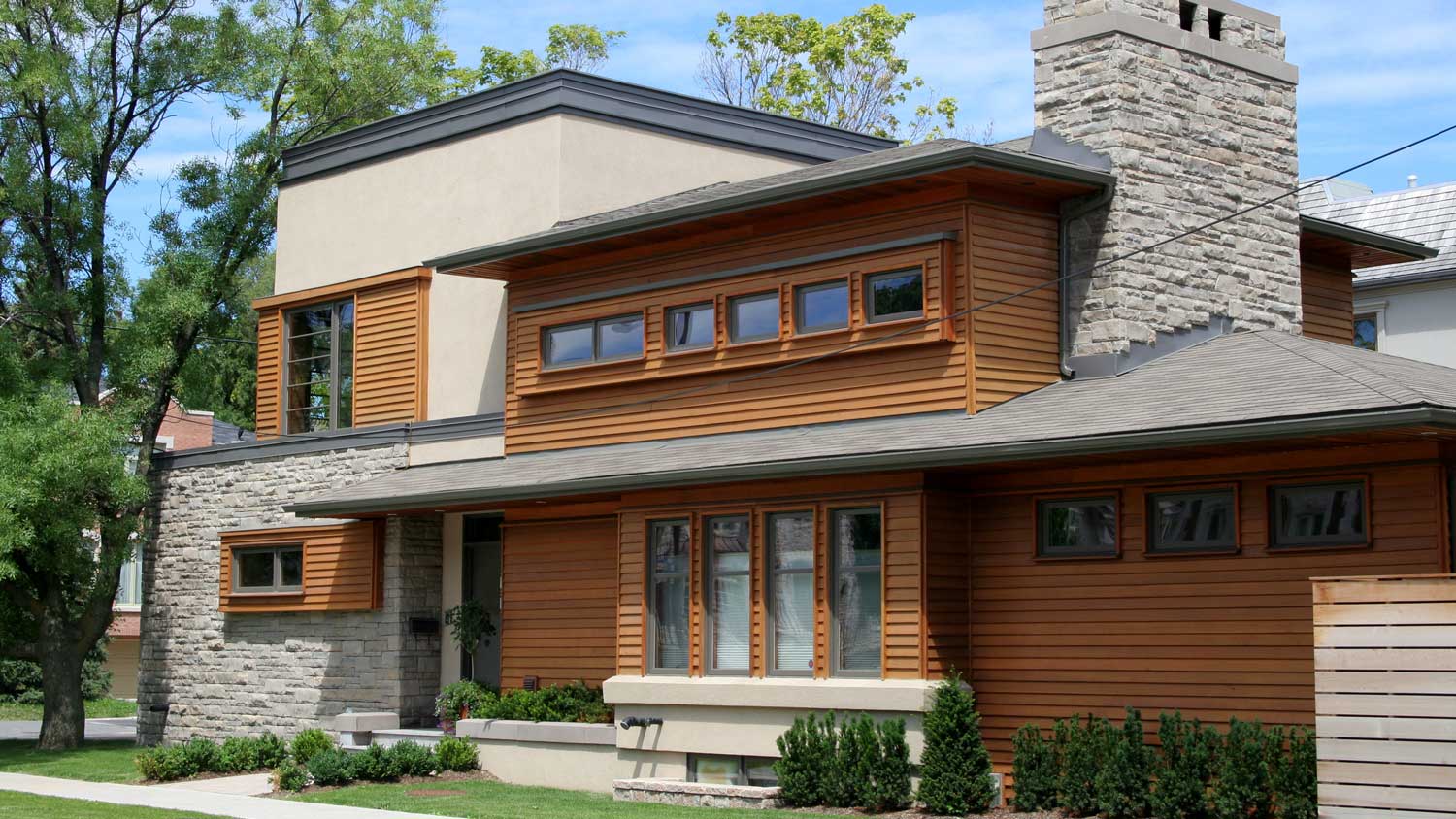 A modern house with cedar siding and a stone chimney