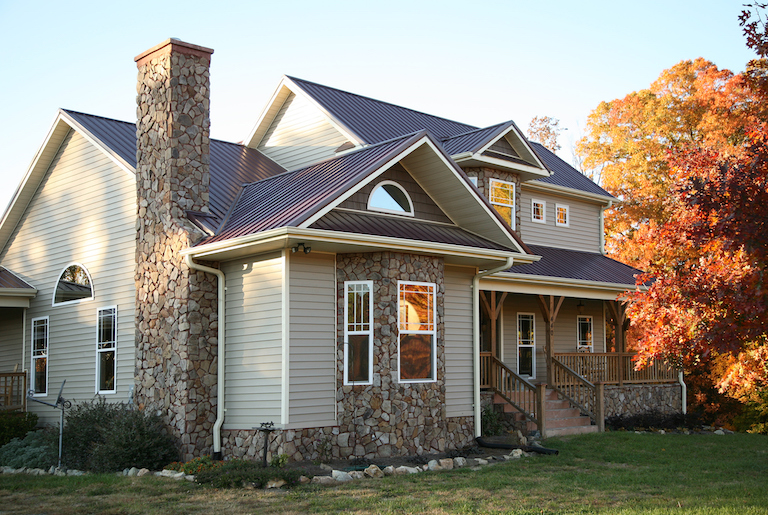 view of house with tan siding, stone accents, and brown metal roof