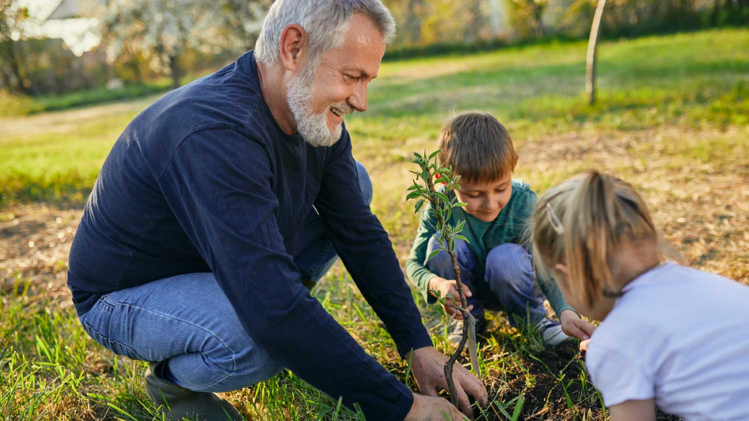 man planting tree with grandchildren at garden