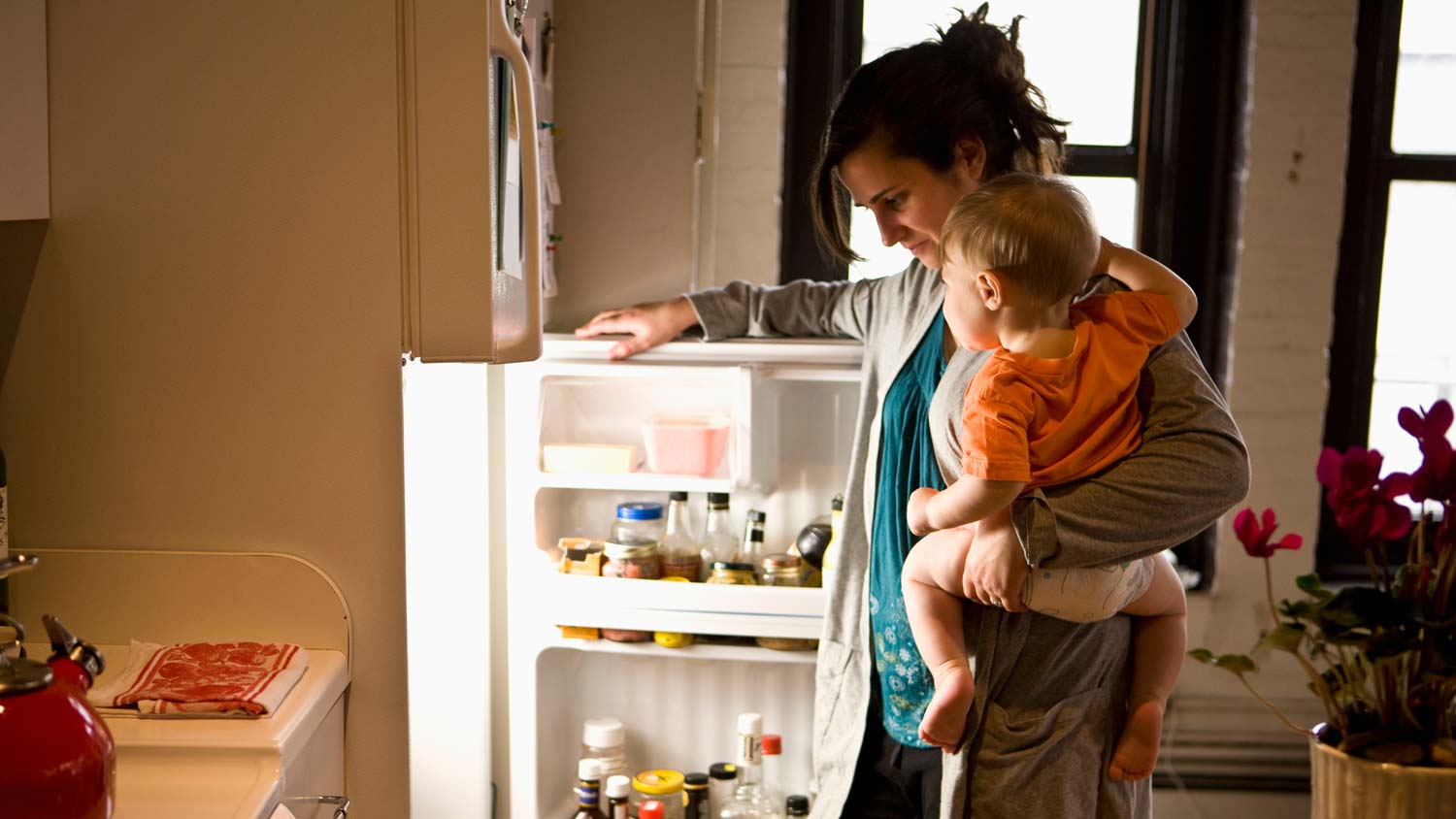 A mother holding her baby looking inside the refrigerator