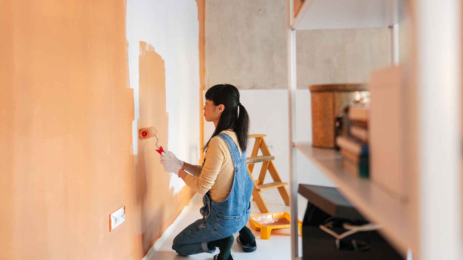 Woman using orange paint to paint an interior wall