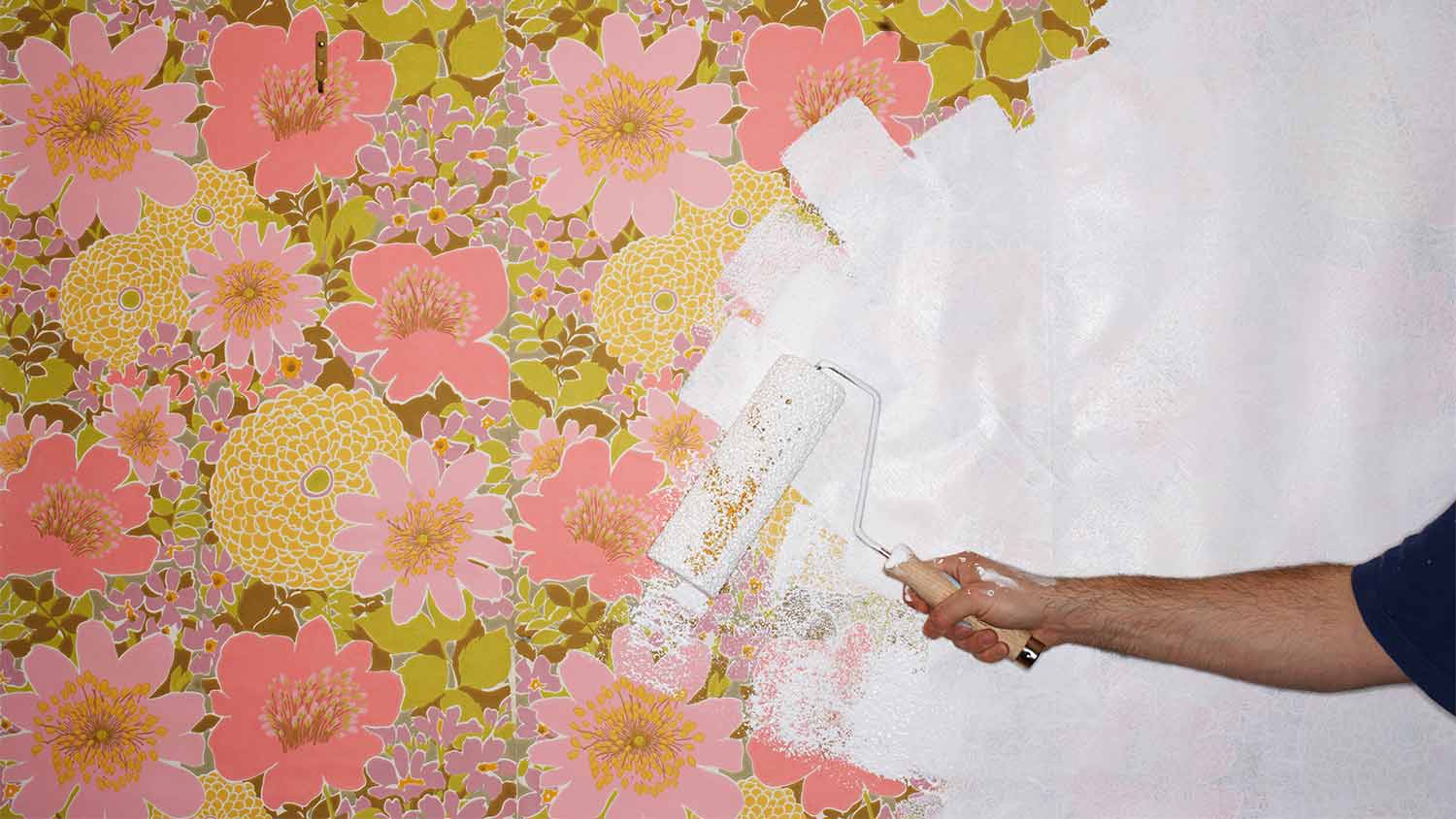 man painting over floral wallpaper