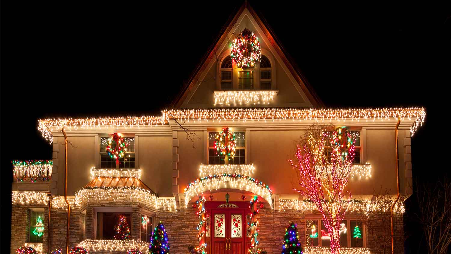 A view of the exterior of a stucco house decorated with Christmas lights