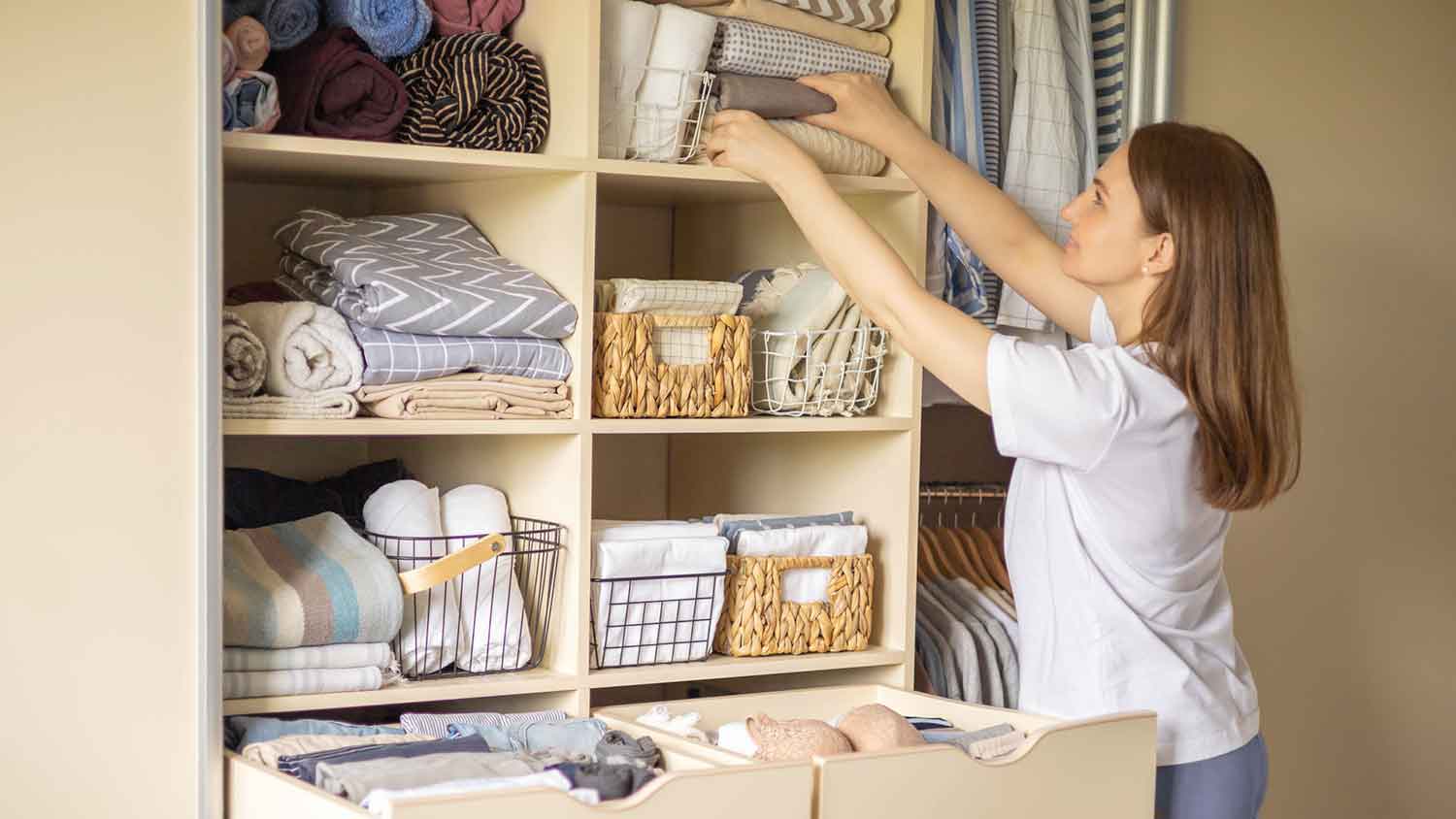 A woman is taking a bed linen from the closet shelf