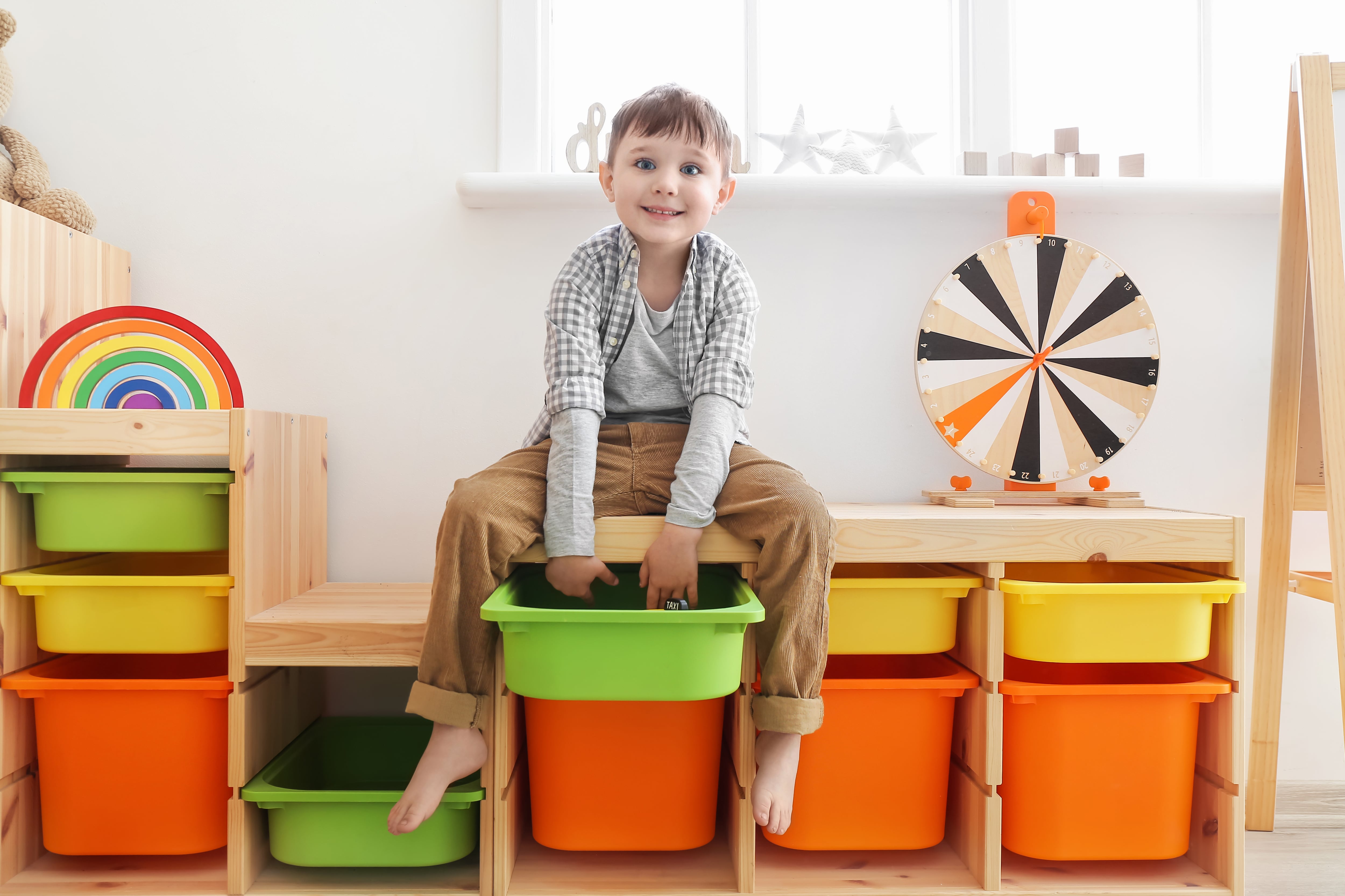 A smiling young boy sitting on top of a wooden shelving unit