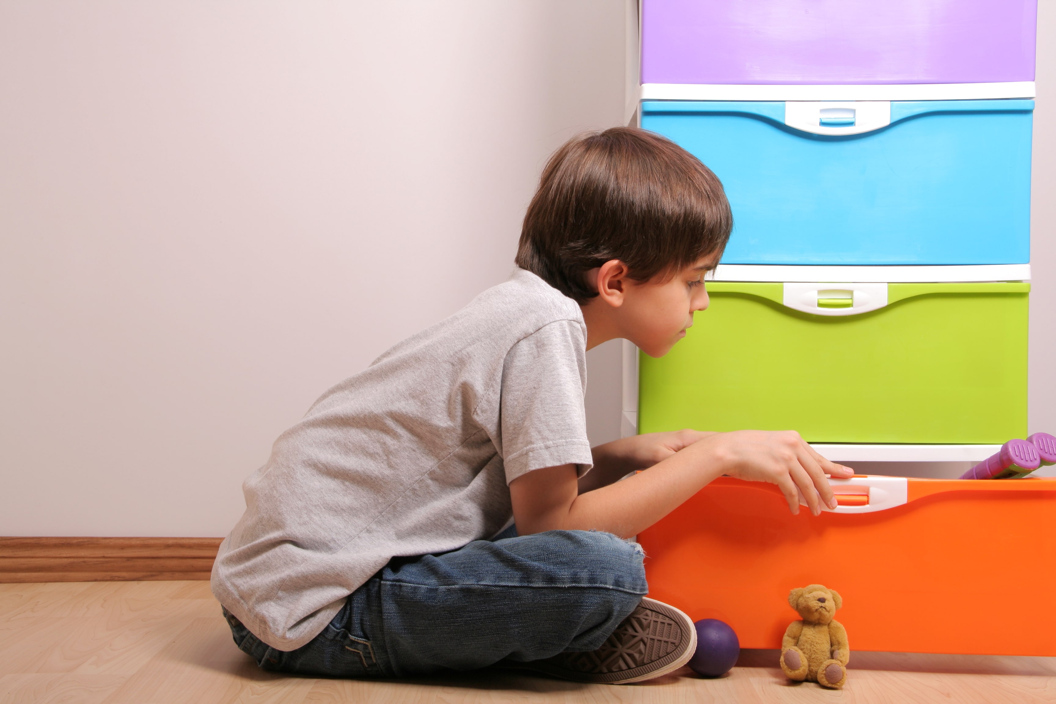 A young boy looking through toys stored in a plastic drawer unit