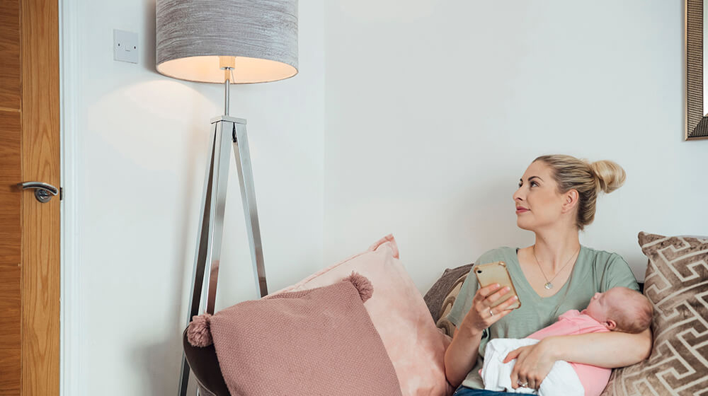 Person looking at a lamp while holding a baby and cellphone