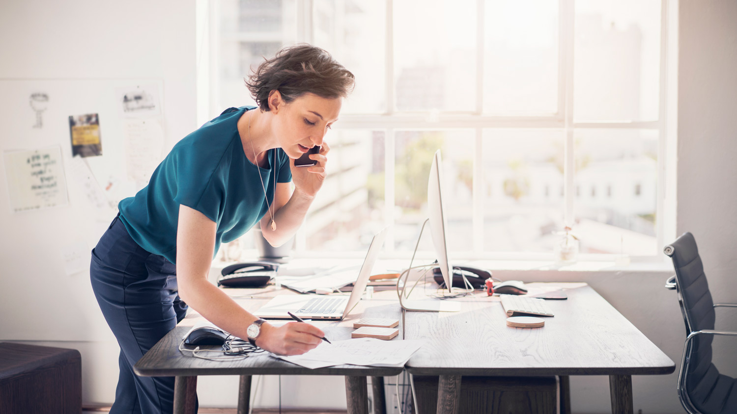 A woman taking notes while talking on the phone