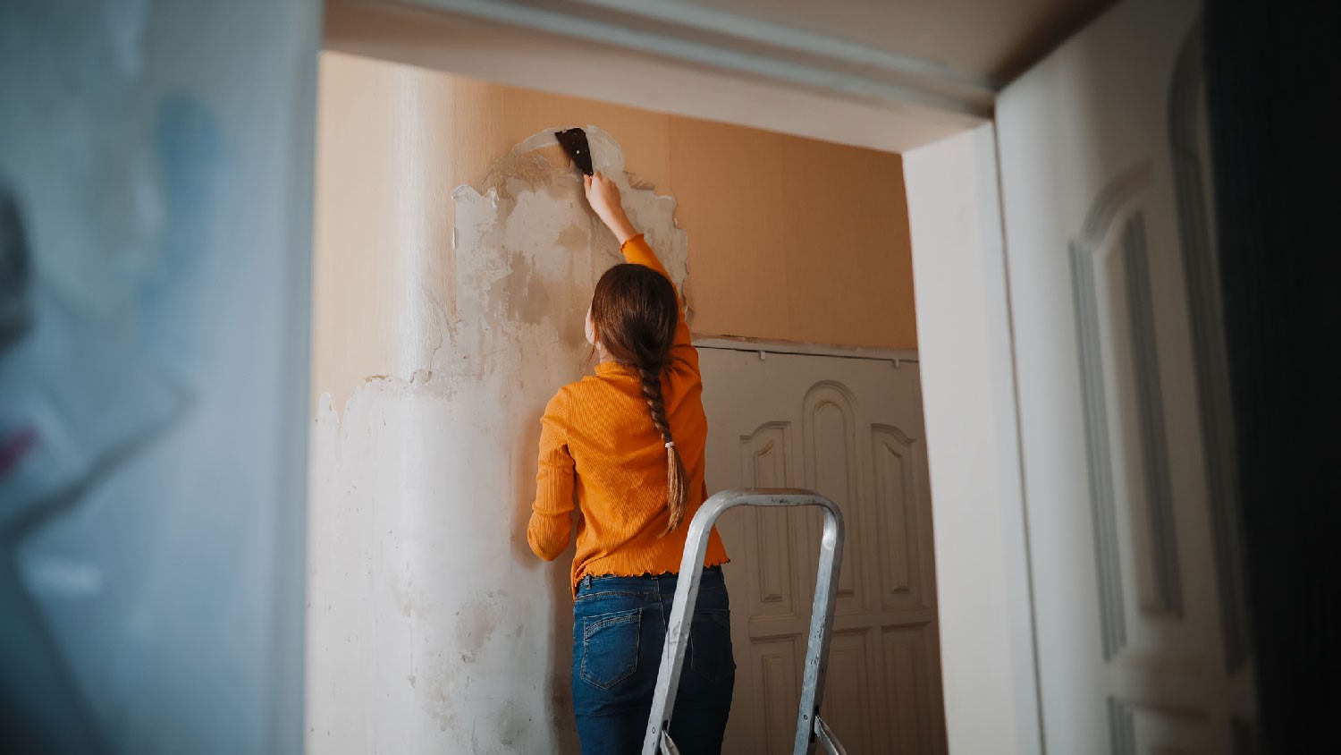 A woman removing wallpaper with a scraper