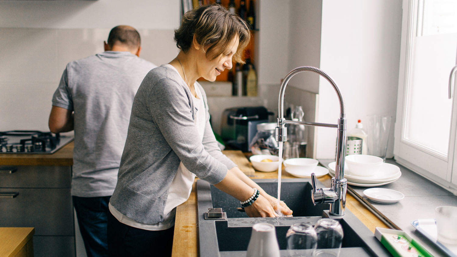 Woman washes dishes under running water at kitchen sink