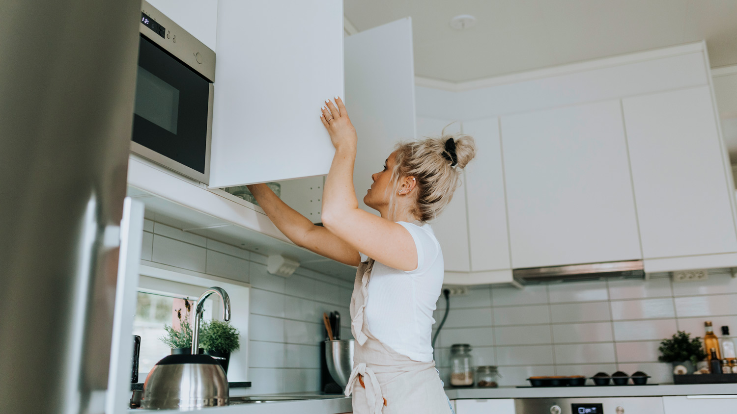 Woman standing in kitchen opening cabinets 
