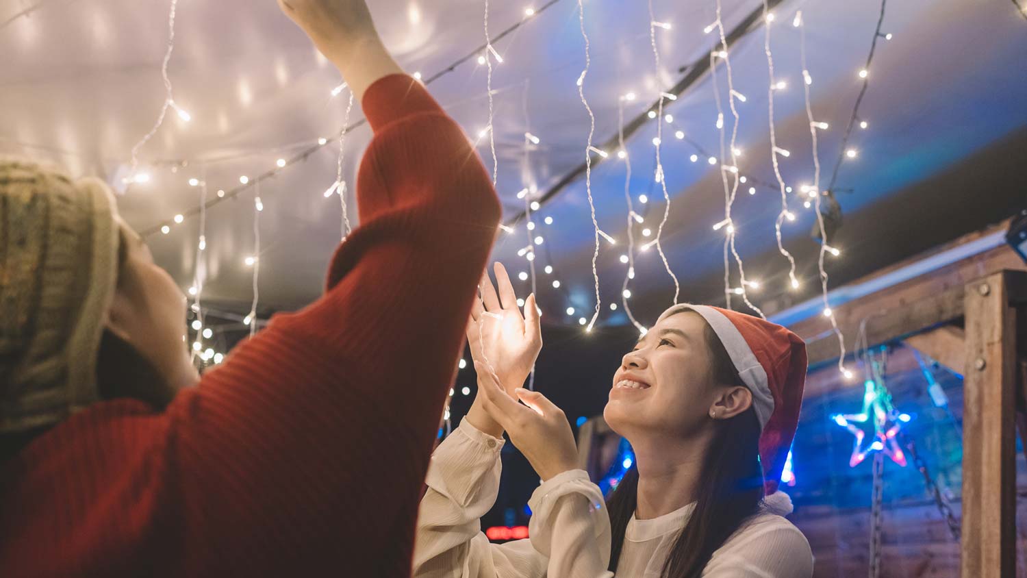Two women hanging Christmas lights from the ceiling